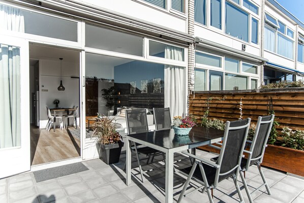A modern outdoor dining area with a glass table and chairs, a wooden fence, and a view of the cityscape.