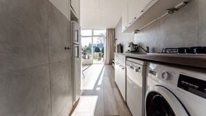 Eine moderne Küche mit eingebauter Waschmaschine und Trockner, einem großen Fenster und Blick ins Freie.