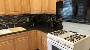 A kitchen with wooden cabinets, a white stove, a black microwave, and a tiled backsplash. - 1bedroom/1 bath      (Oneonta)