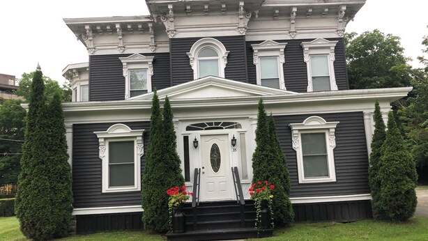 A two-story Victorian-style house with a symmetrical facade, a central entrance with a white door, and two tall, narrow trees flanking the front. - 1bedroom/1 bath      (Oneonta)