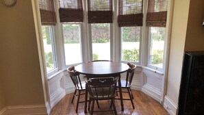 A dining area with a round table and four chairs, large windows with blinds, wooden flooring, and a clock on the wall. - 1bedroom/1 bath      (Oneonta)
