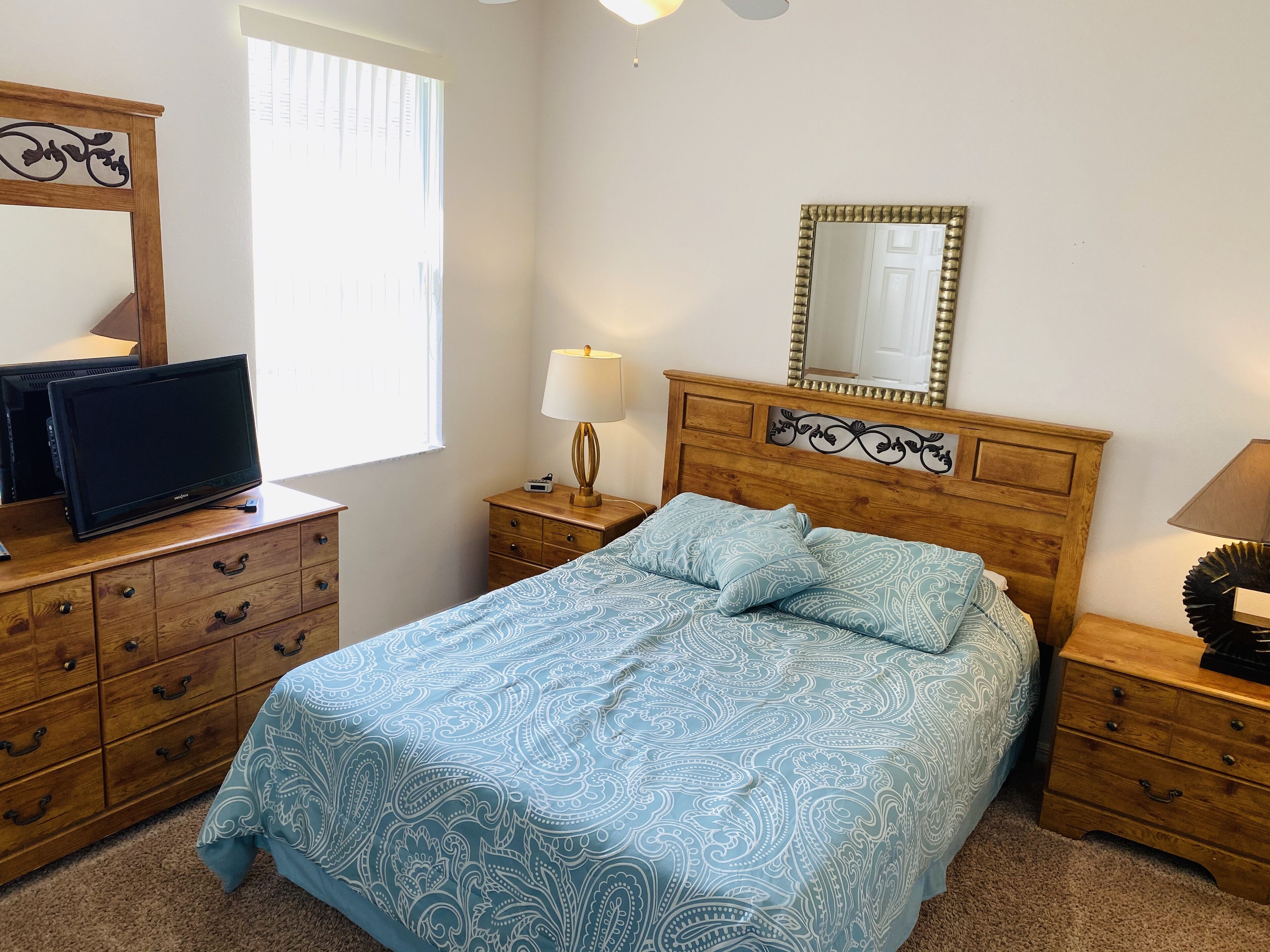 A bedroom with a bed, a dresser, a nightstand, a lamp, a television, and a mirror.