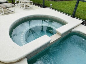 A swimming pool with a built-in hot tub, surrounded by a white tiled deck and a grassy area.