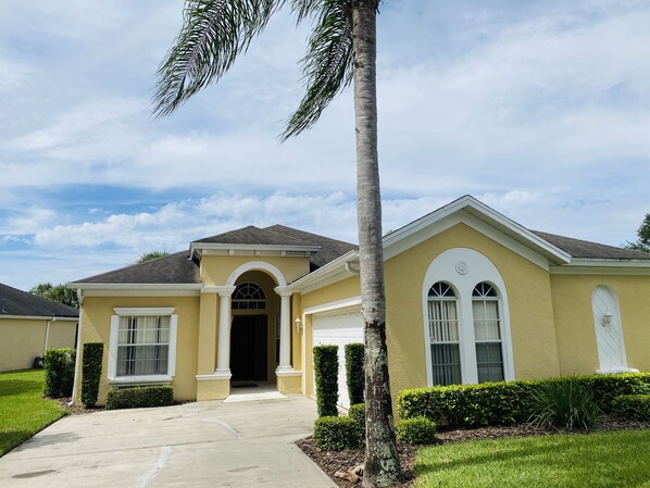 A two-story house with a yellow facade, a front entrance with an archway, and a driveway leading to the door.