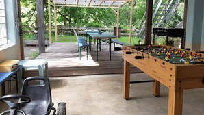 A covered outdoor area with a foosball table, a table with chairs, and a patio table. - dasokerhaus.com (Altenau)