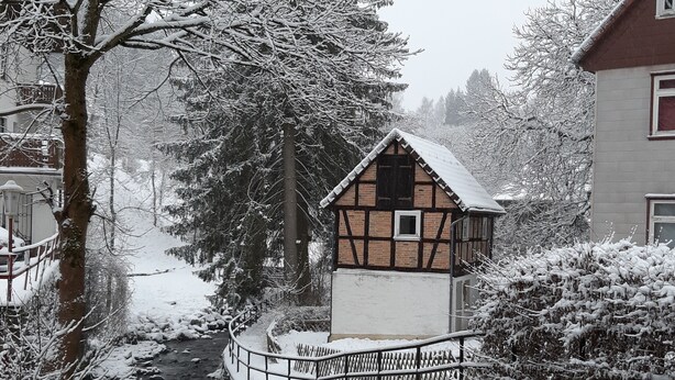 A traditional half-timbered house with a small balcony, surrounded by snow-covered trees and a river. - dasokerhaus.com (Altenau)