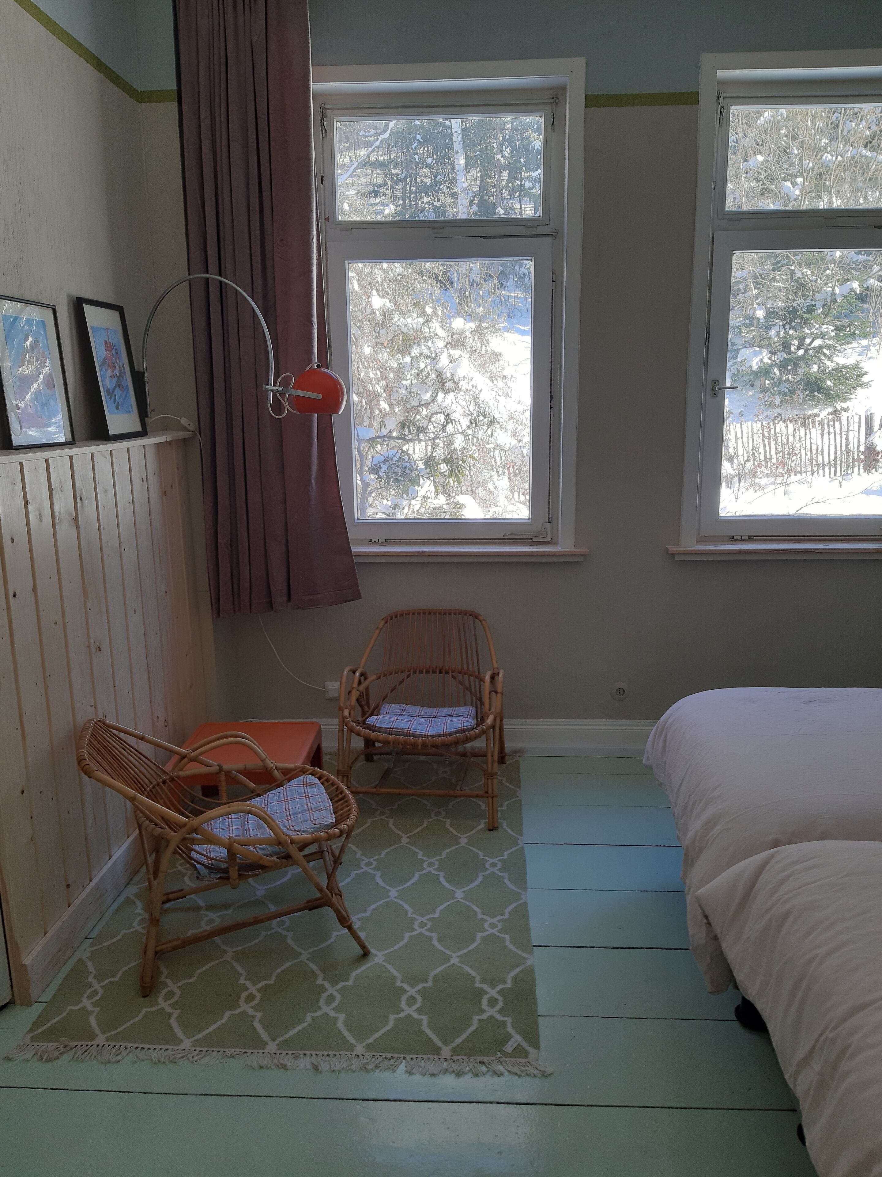 Ein Schlafzimmer mit zwei Korbstühlen, einem Bett, einem Fenster mit Blick auf schneebedeckte Bäume und einem gemusterten Teppich.