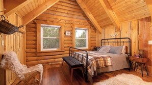 Ein Schlafzimmer in einer Blockhütte mit Bett, Bank und zwei Fenstern.