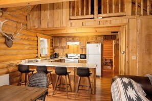 A log cabin interior with a kitchen, dining area, and a living room.