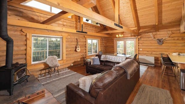 Ein Holzblockhaus mit Kamin, Holzwänden, einer Ledersofa und einem Essbereich.
