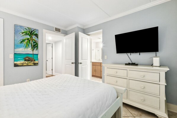 A bedroom with a bed, a TV, a dresser, and a painting of a beach scene. - Pet Friendly | Ground Level Sailmaker Villa | Private Covered Patio | Close to Pool (Fernandina Beach)