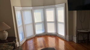 Une pièce dotée d’une fenêtre en saillie d’angle, d’un plancher en bois, d’un téléviseur à écran plat et d’une lampe.