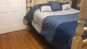 Une chambre avec un plancher en bois, un lit doté d’une tête de lit et une porte blanche.