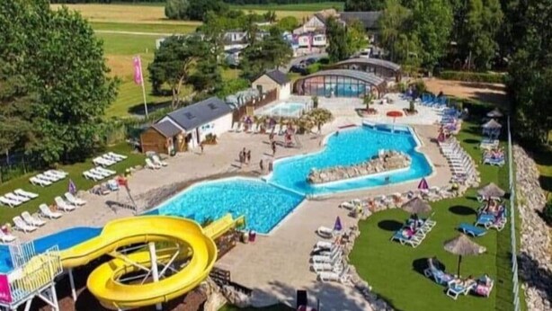 Un resort con una grande piscina, uno scivolo acquatico e lettini prendisole.