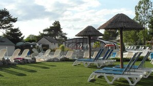 Area piscina con lettini e ombrelloni, circondata da un prato curato e un edificio con facciata in vetro.