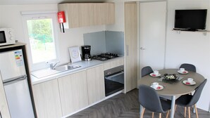 Una cucina compatta con forno a microonde, macchina del caffè e forno. C'è un tavolo da pranzo con sedie e un televisore fissato alla parete.