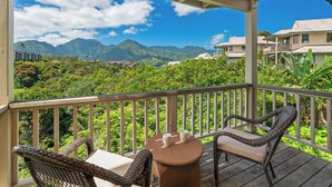Un espacio al aire libre cubierto con mobiliario de mimbre y una mesa, con vistas a un paisaje exuberante con montañas y edificios.