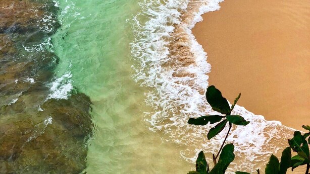 Una playa con agua turquesa cristalina, una orilla arenosa y rocas a la vista.