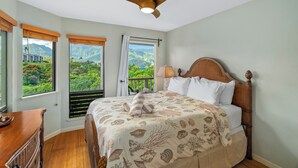 Un dormitorio con cama, ventilador de techo, mesita de noche y vistas a montañas y vegetación.