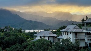 Vista costera con una cadena montañosa al fondo, una masa de agua y varios edificios con balcones.