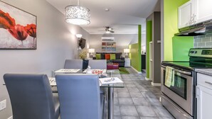 Een moderne keuken met een groene accentmuur, een eethoek met een glazen tafel, en een woonkamer met een bank en een televisie.