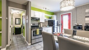 Een moderne keuken met een eethoek, met roestvrijstalen apparatuur, een rode deur en een groene accentmuur.