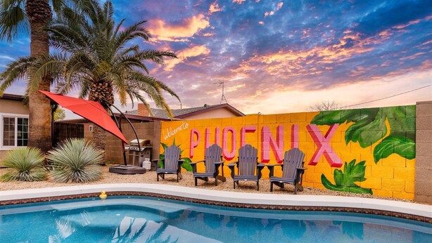Een zwembadgedeelte met een muurschildering met de tekst 'Welcome to PHOENIX' en Adirondack-stoelen.