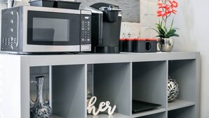 Een keukenhoek met een magnetron, koffiezetapparaat en een plank met decoratieve objecten.