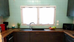 A kitchen with dark cabinets, a white window, a sink, and a microwave. - La Borieta (Labastide-de-Penne)