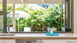 A kitchen with a window view of a garden, a wine bottle, and glasses on a tray. - Inner Sanctum in Long Beach (LONG BEACH)