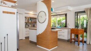 A modern kitchen with a central island, wooden accents, a clock, and a view of greenery outside. - Inner Sanctum in Long Beach (LONG BEACH)