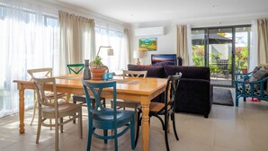 A well-lit living room with a dining area, a sofa, and a TV. There is a window with curtains and a painting on the wall. - Inner Sanctum in Long Beach (LONG BEACH)