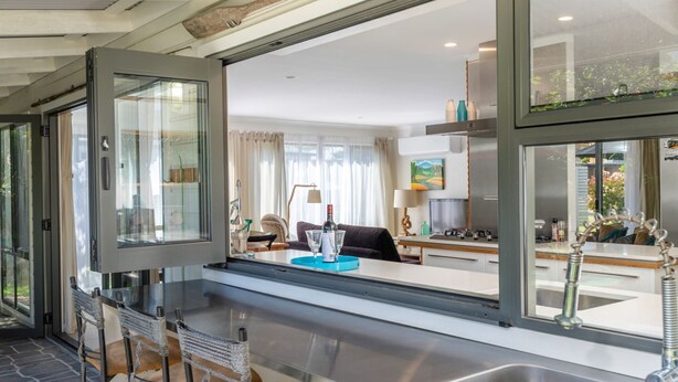 A modern kitchen with a large window, a dining area with a table and chairs, and a living room with a sofa and a painting. - Inner Sanctum in Long Beach (LONG BEACH)