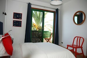 A hotel room with a bed, a red chair, a table with chairs, a window with curtains, and a wall-mounted mirror. - CASA DEL MAR, ALCALA—SLEEPS 6 (alcala, Guia de Isora,)