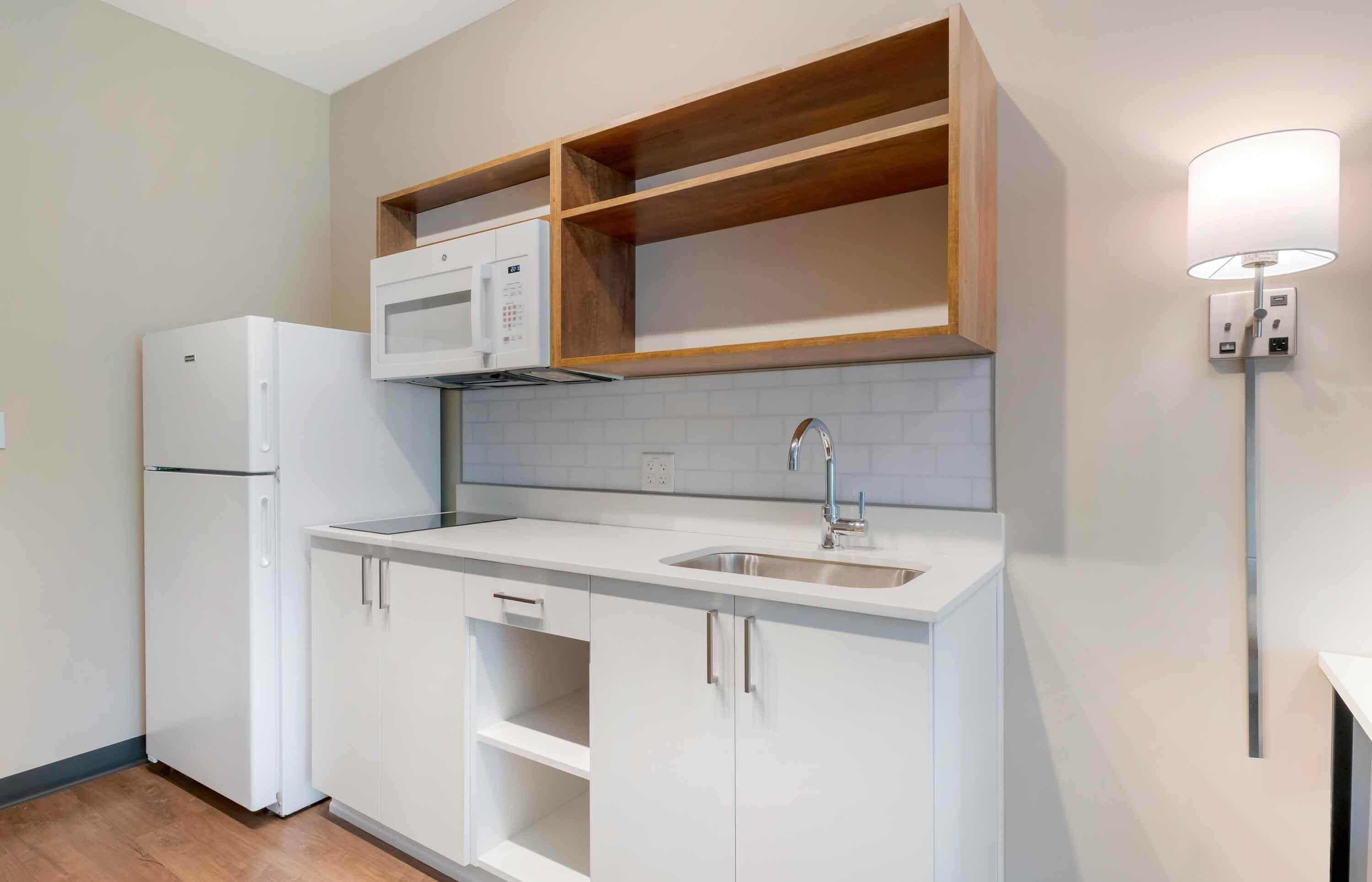 Una cocina compacta con muebles blancos, un microondas integrado y un lavamanos.