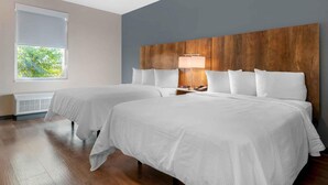 Une chambre d’hôtel avec deux lits, une tête de lit en bois, une fenêtre avec des stores et une table de chevet avec une lampe.