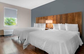 Habitación de hotel con dos camas, cabecero de madera, ventana con persianas y mesita de noche con lámpara.