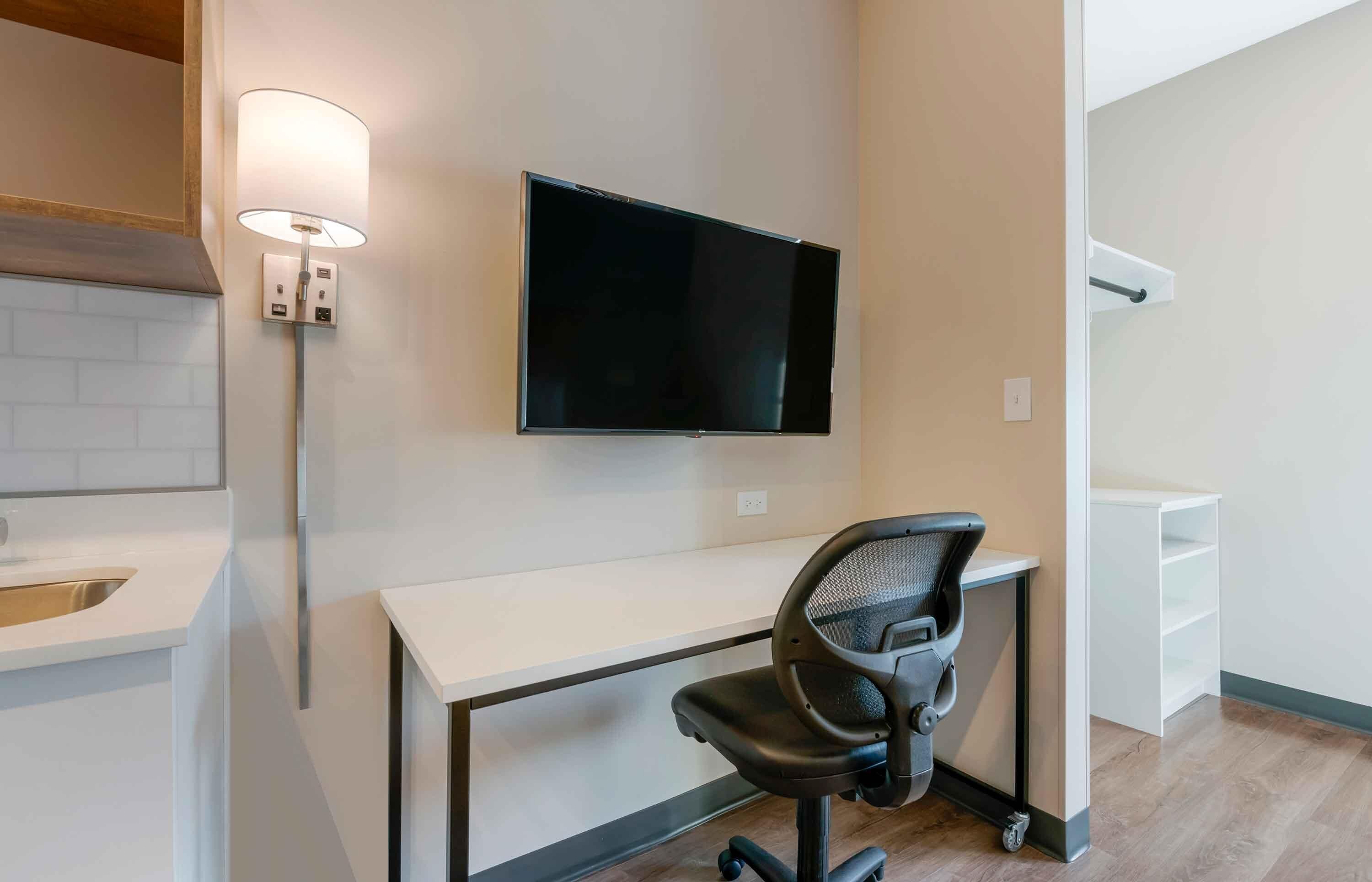 A modern office space with a desk, chair, and mounted flat-screen TV.