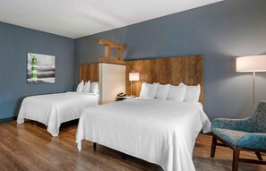 Habitación de hotel con dos camas, cabecero de madera, mesita de noche, lámpara y una silla.