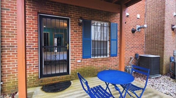 Un edificio de ladrillo con una puerta azul, una ventana con contraventanas azules y una mesa y sillas al exterior.