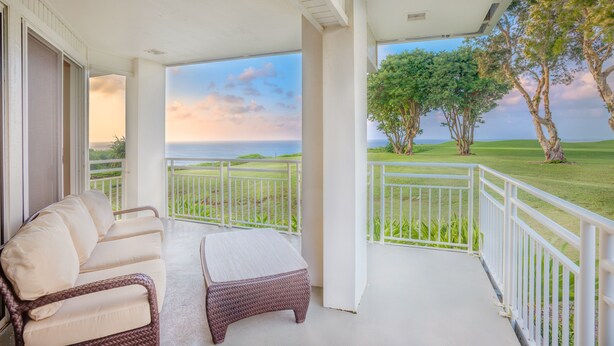 Un balcone con divano e poggiapiedi in vimini, con vista su un campo da golf e sull'oceano.