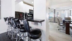 A modern kitchen with a bar area, bar stools, and a dining area with a sofa and table. - Total Oasis - 8BR Resort Compound, Pool & Tiki Bar, Sleeps 30, Near Cruise Port (Hollywood)