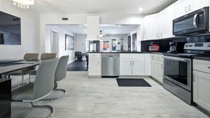 A modern kitchen with white cabinets, stainless steel appliances, and a dining area with a table and chairs. - Total Oasis - 8BR Resort Compound, Pool & Tiki Bar, Sleeps 30, Near Cruise Port (Hollywood)
