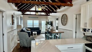 Amplia sala de estar con techo alto, comedor y cocina con armarios blancos.