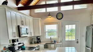 Una cocina con armarios blancos, una isla grande con taburetes, microondas, cafetera y refrigerador.