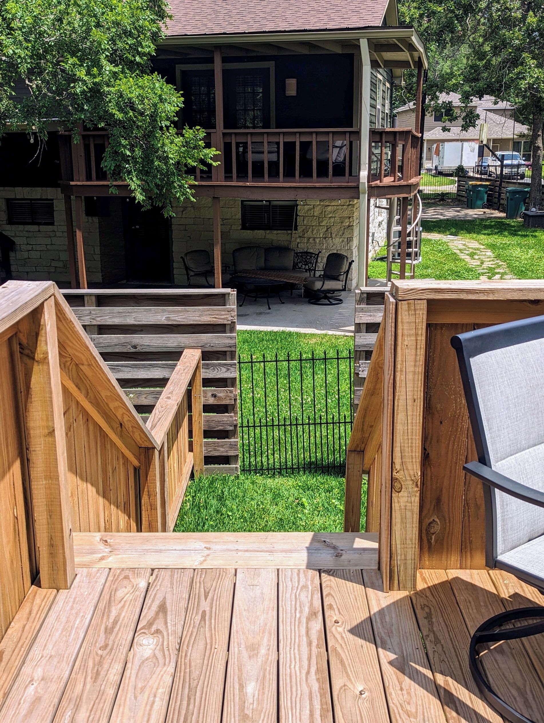 A wooden deck with a view of a house, a patio with outdoor furniture, and a fenced yard.