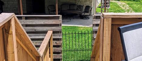 A wooden deck with a view of a house, a patio with outdoor furniture, and a fenced yard.