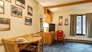 A dining area with a wooden table set for four, a television on a wooden stand, and a red chair. - Silver Creek 1104  Studio Sleeps 3,  Slope Side (Snowshoe)