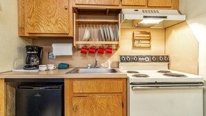 A compact kitchen with wooden cabinets, a white stove, a black refrigerator, and a coffee maker. - Silver Creek 1104  Studio Sleeps 3,  Slope Side (Snowshoe)