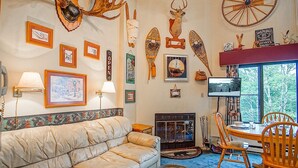 A cozy room with a sofa, a fireplace, a dining table with chairs, and various wall decorations including animal heads and a clock. - Silver Creek 5216 - The Winter`s Wonderland 2 Br Condo (Snowshoe)